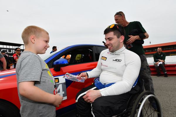 Michael, in his wheelchair, greets a young fan beside the car, 2018