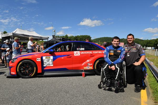 Michael in his wheelchair beside the #54 Audi on the grid, with crew member Josh Gibbs kneeling next to him, 2018