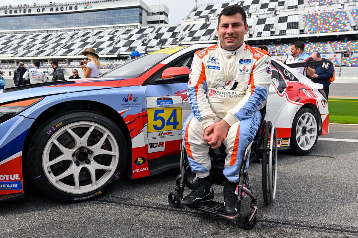Michael Johnson in his racing suit, seated in his wheelchair in front of the #54 Hyundai Elantra N TCR